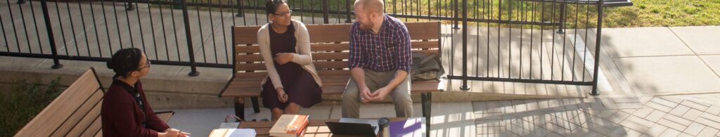 Students seated on a bench talking on a fall day.